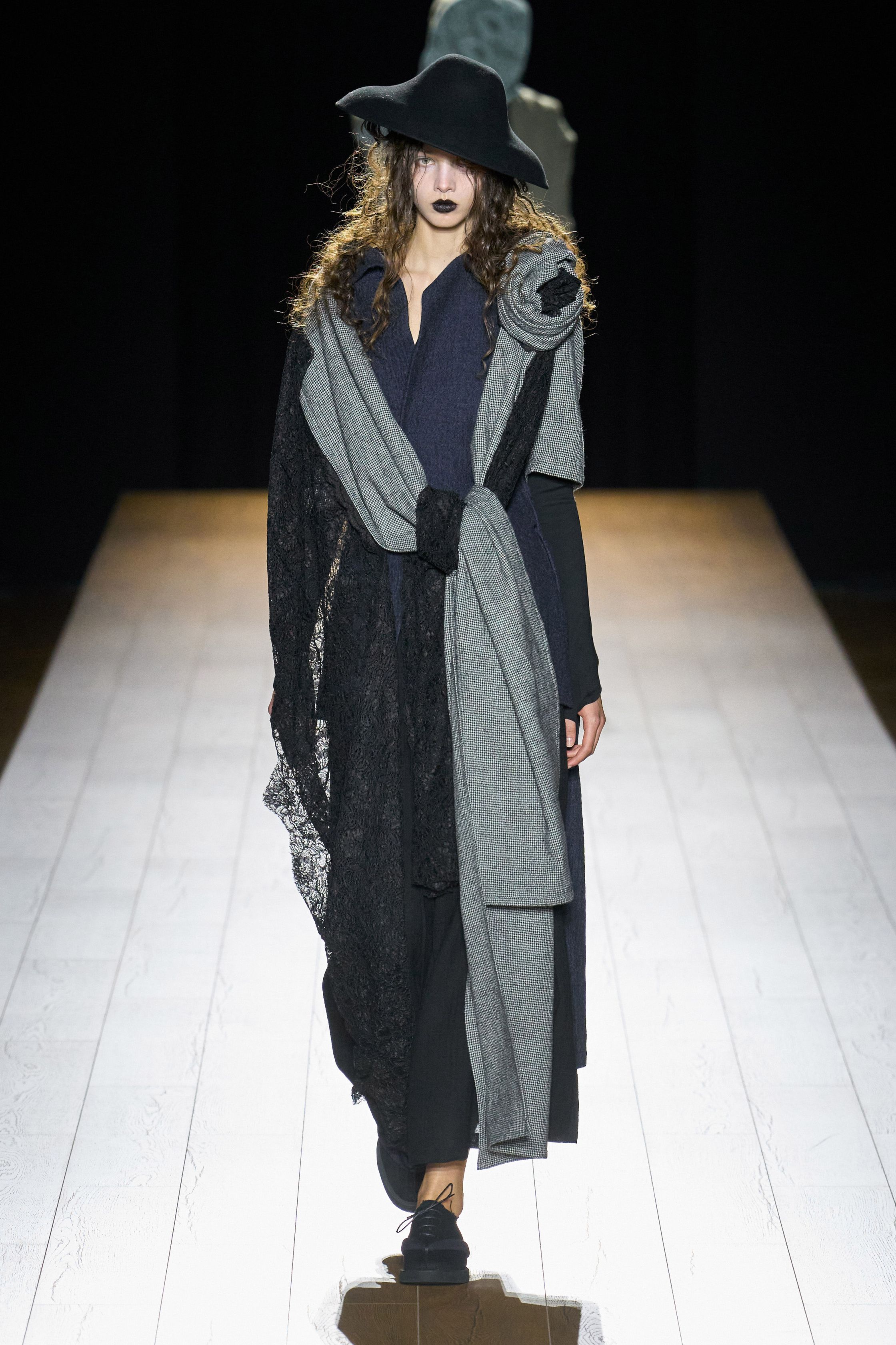 Yohji Yamamoto 本季依然延续标志性的黑色哲学：宽松层叠轮廓、和服式结构与手工拼接面料形成一种诗意而深沉的东方美学。夸张头饰与飘逸衣摆让整场秀像一场黑色戏剧，既神秘又极具艺术感-顽石频道趋势研究